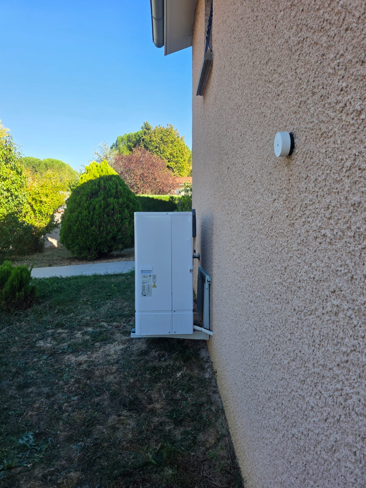 Unité extérieure de pompe à chaleur et traversée de mur obturée par un cache blanc