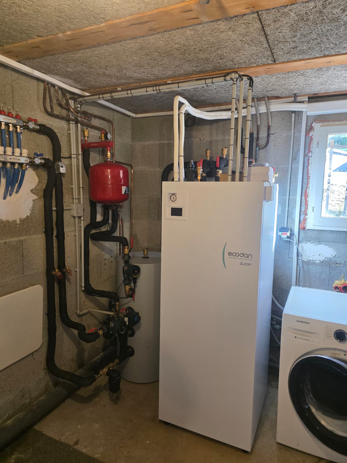 Vue d’ensemble du local technique : module intérieur, ballon tampon, vase d’expansion et collecteur de plancher chauffant