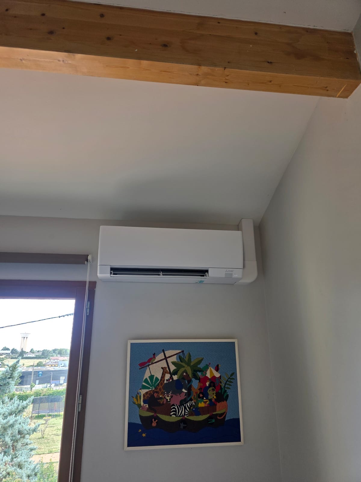 Split mural de climatisation posé sous une poutre apparente, au-dessus d’un tableau